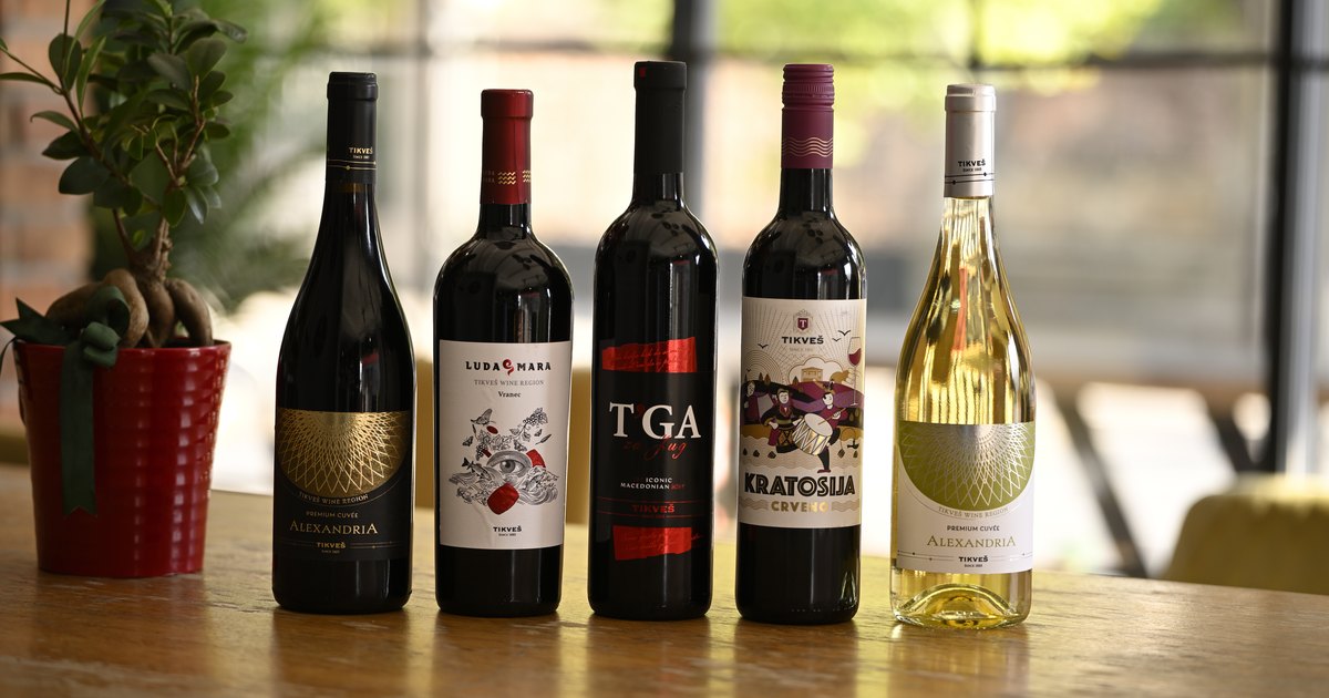 Five Tikveš bottles in a row on a wooden table: Alexandria Cuvée red, Luda Mara Vranec, T'ga za Jug, Kratošija and Alexandria Cuvée white.