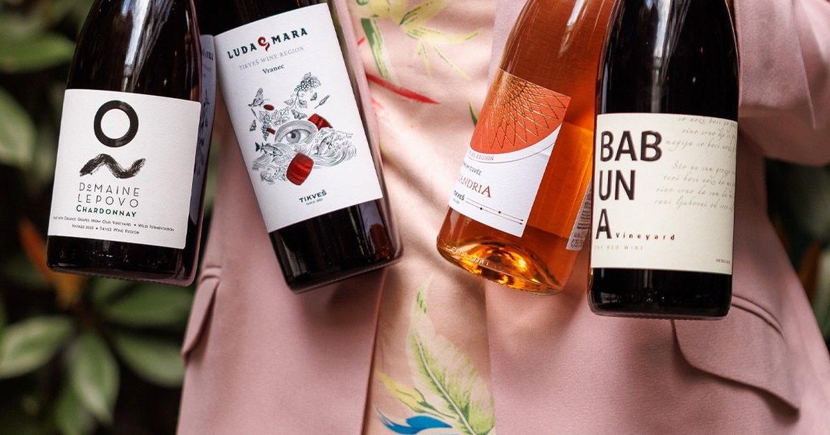 A woman in a pink jacket holding four bottles of wine, a white, two reds and a rosé, from the Tikveš range.