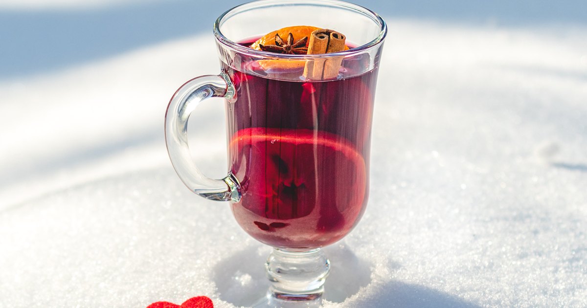 A glass mug of mulled wine with orange, star anise and cinnamon standing in fresh snow.