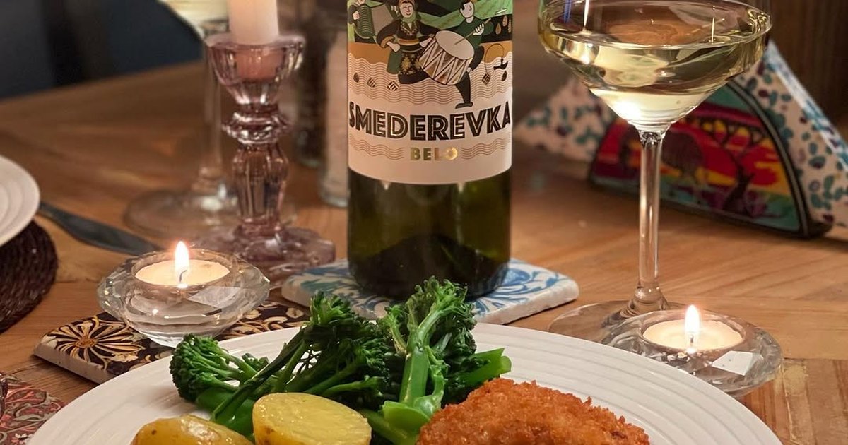 A bottle of Tikveš Smederevka white wine on a candlelit dinner table beside a glass, with breaded chicken, potatoes and broccoli.