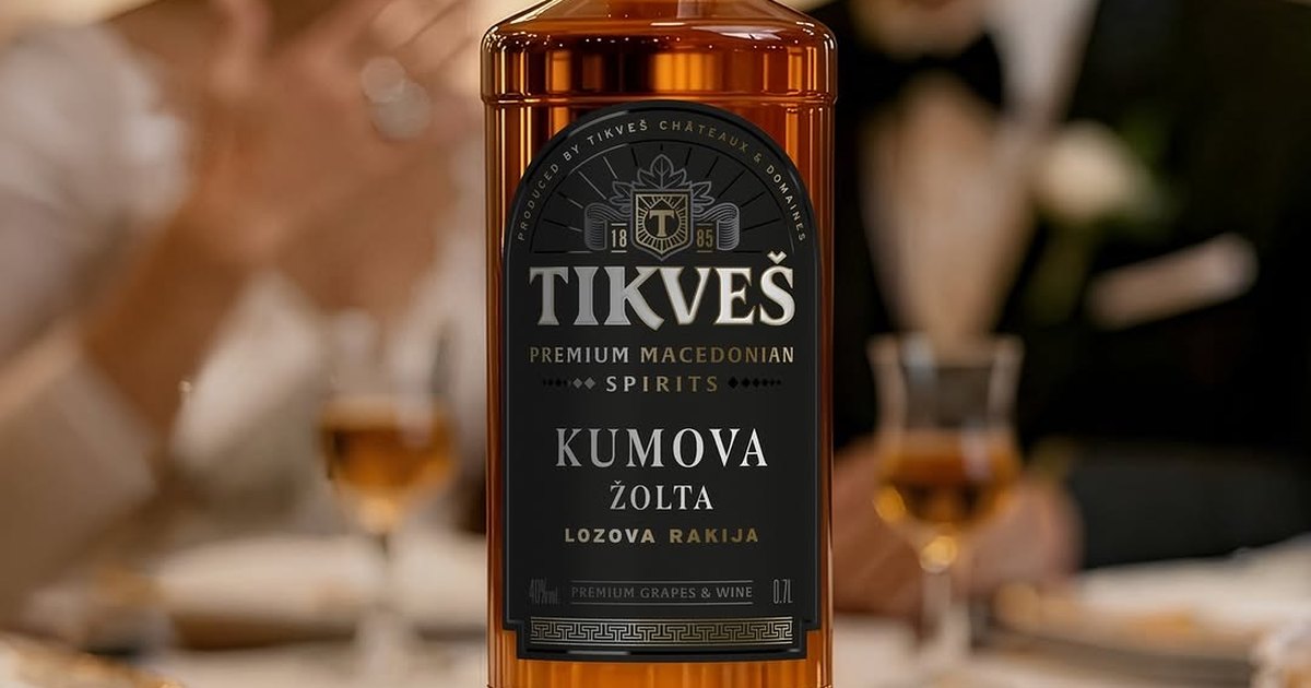 A bottle of Tikveš Kumova Žolta grape rakija on a wedding table, with a couple and two glasses behind.