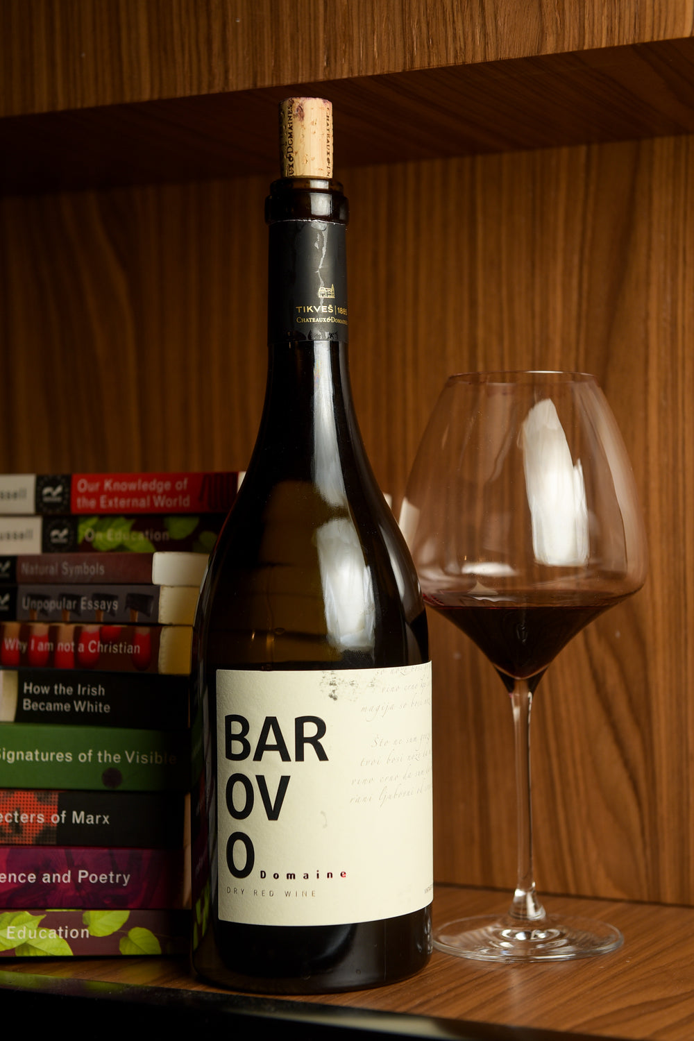 Bottle of Barovo Red standing beside a poured glass of red wine on a wooden shelf