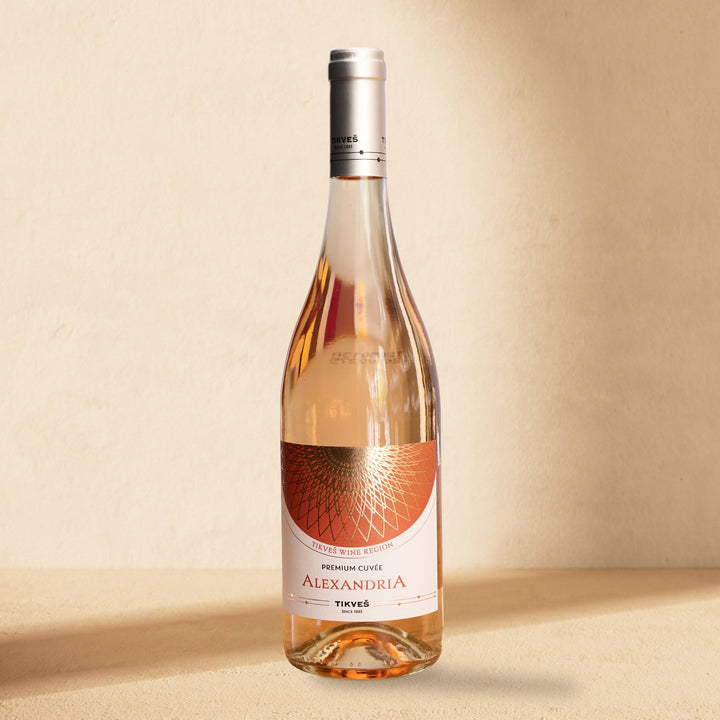 A bottle of Alexandria Premium Cuvée Rosé standing against a cream wall in soft window light