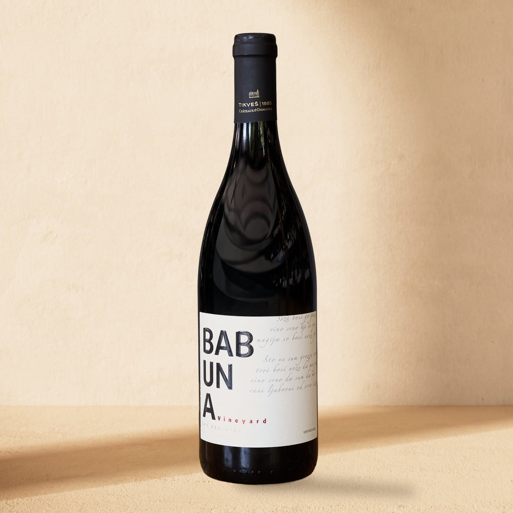 A bottle of Babuna Red standing against a cream wall in soft window light