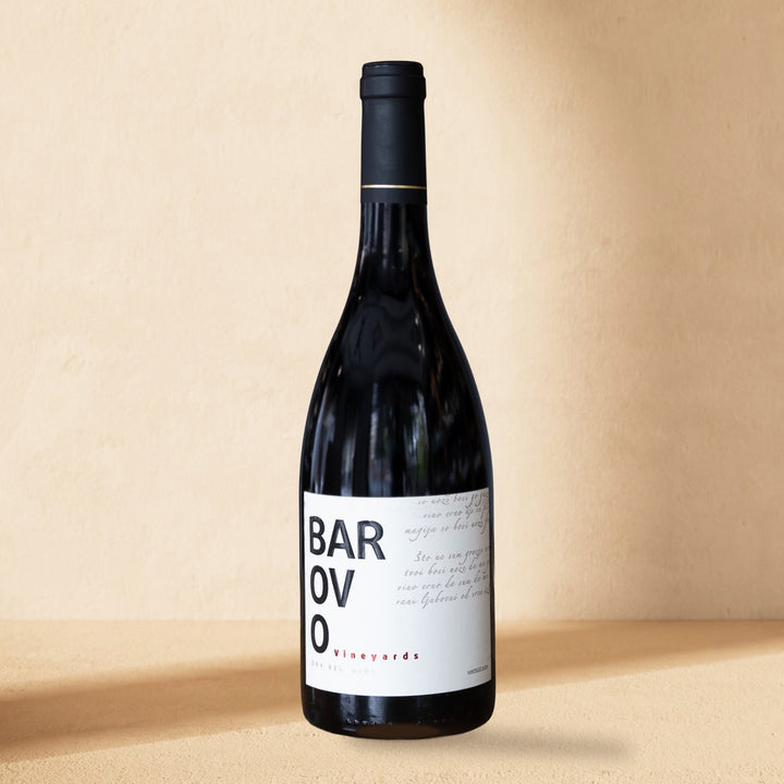 A bottle of Barovo Red standing against a cream wall in soft window light