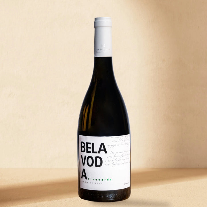 A bottle of Bela Voda White standing against a cream wall in soft window light