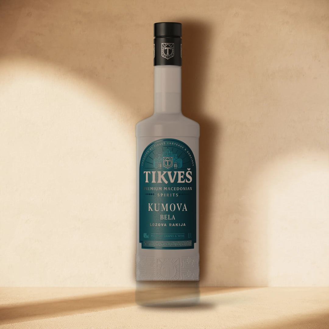 A bottle of Kumova Bela rakija standing against a cream wall in soft window light
