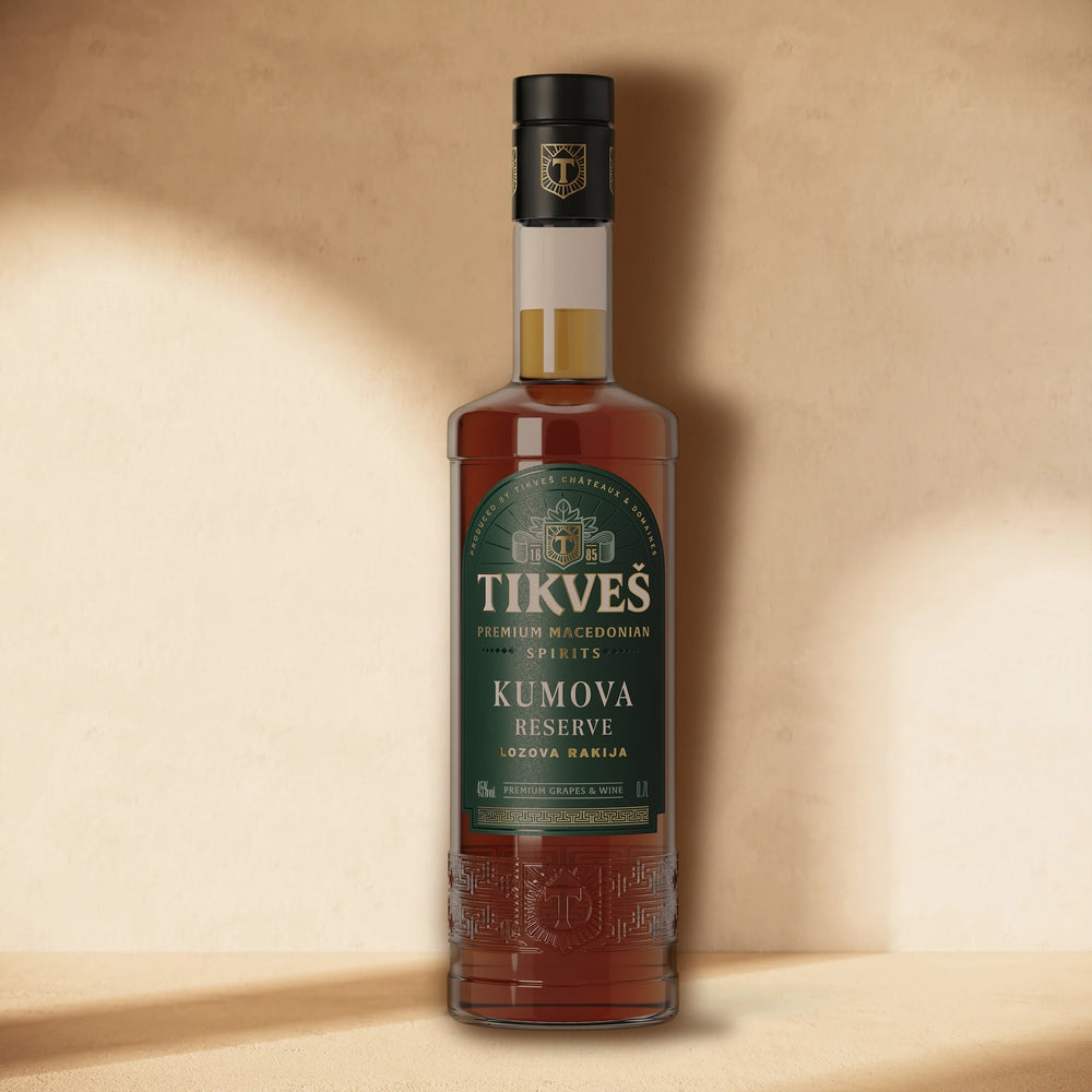 A bottle of Kumova Reserve rakija standing against a cream wall in soft window light