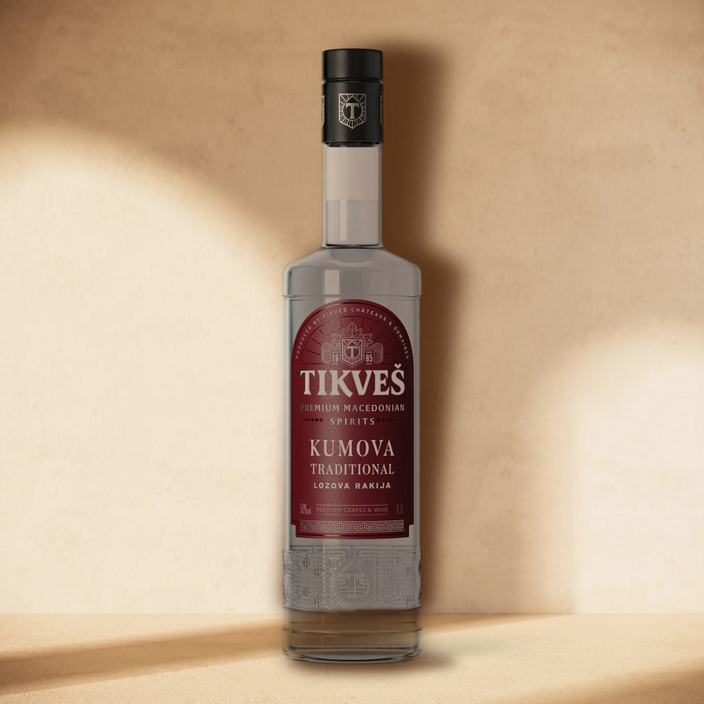 A bottle of Kumova Traditional rakija standing against a cream wall in soft window light