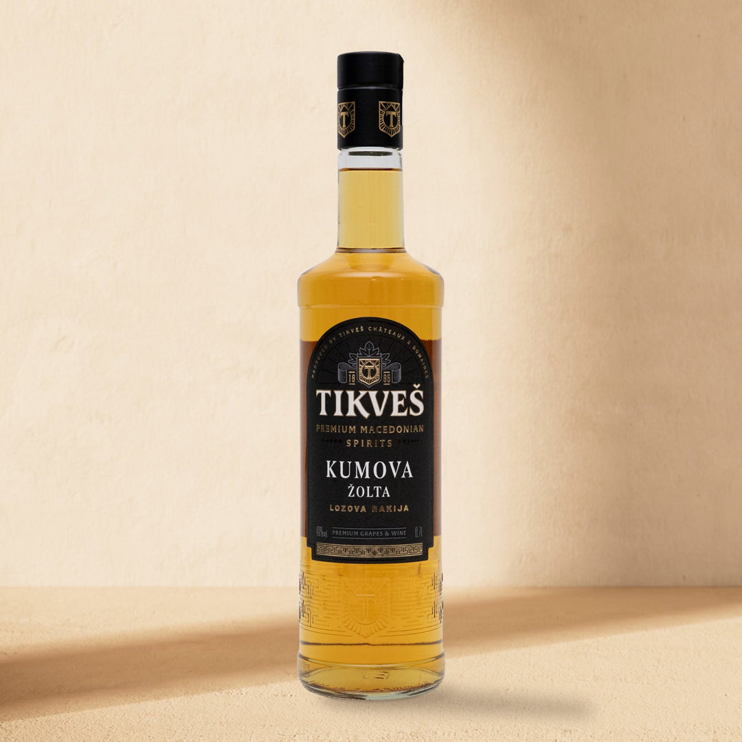 A bottle of Kumova Žolta rakija standing against a cream wall in soft window light
