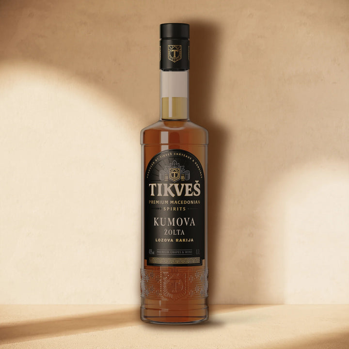 A bottle of Kumova Žolta rakija standing against a cream wall in soft window light