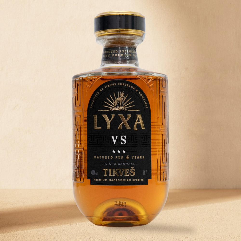 A bottle of LYXA VS grape brandy standing against a cream wall in soft window light
