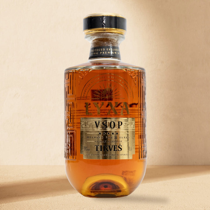 A bottle of LYXA VSOP grape brandy standing against a cream wall in soft window light