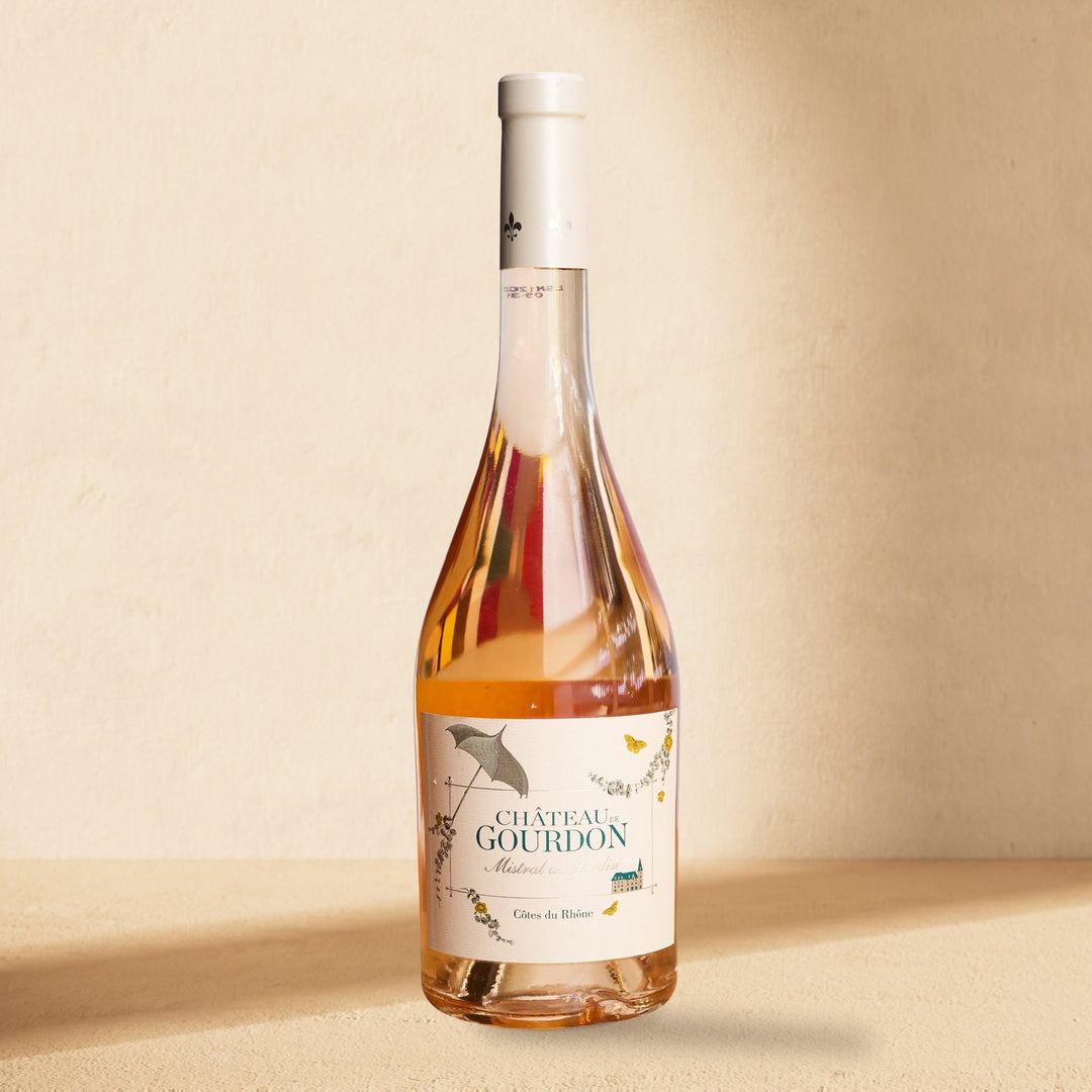 A bottle of Château de Gourdon Mistral au Jardin rosé standing against a cream wall in soft window light