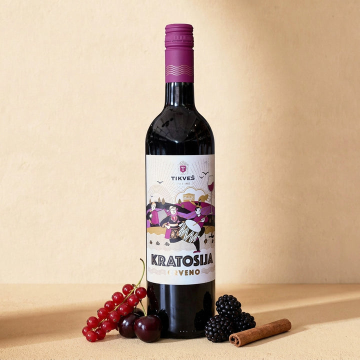 A bottle of Kratošija on a warm cream surface with redcurrants, dark cherries, blackberries and a cinnamon stick