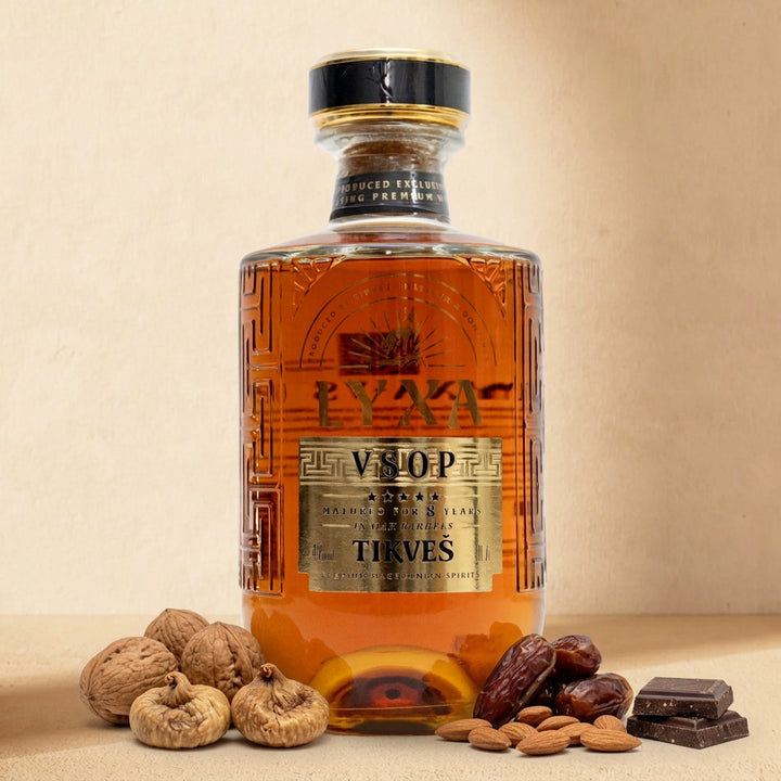 A bottle of LYXA VSOP grape brandy on a warm cream surface with walnuts, dried figs, dates, almonds and dark chocolate
