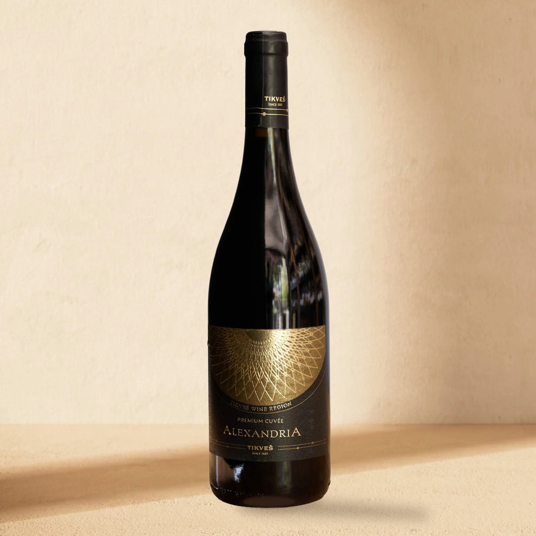 A bottle of Alexandria Premium Cuvée Red standing against a cream wall in soft window light